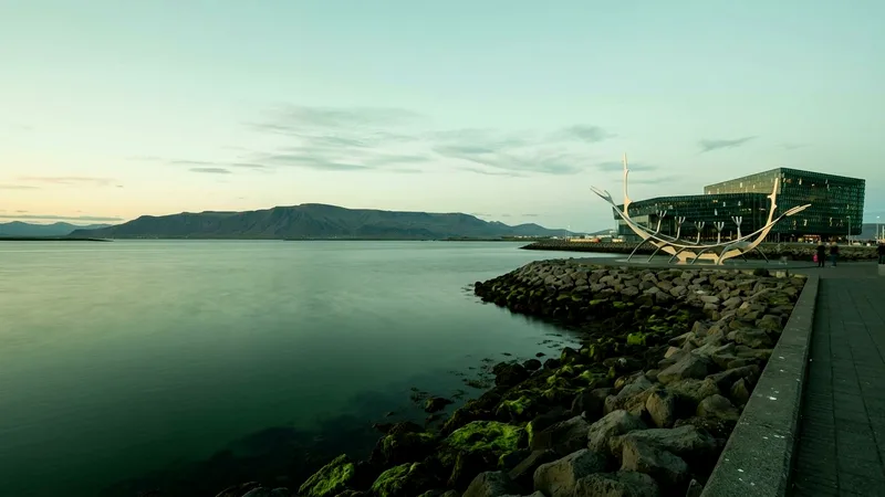 Sun Voyager sculpture and Harpa concert hall beside calm bay with Mount Esja behind