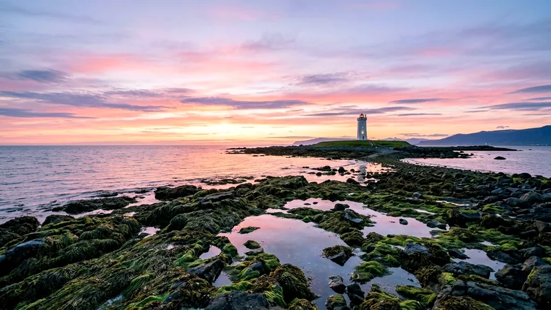 Grótta lighthouse on rocky peninsula with tidal pools under pastel summer sky
